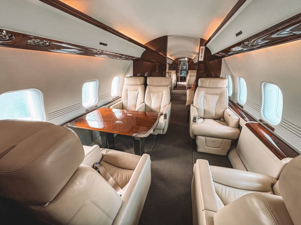 Private jet cabin with cream leather seats and a wood table